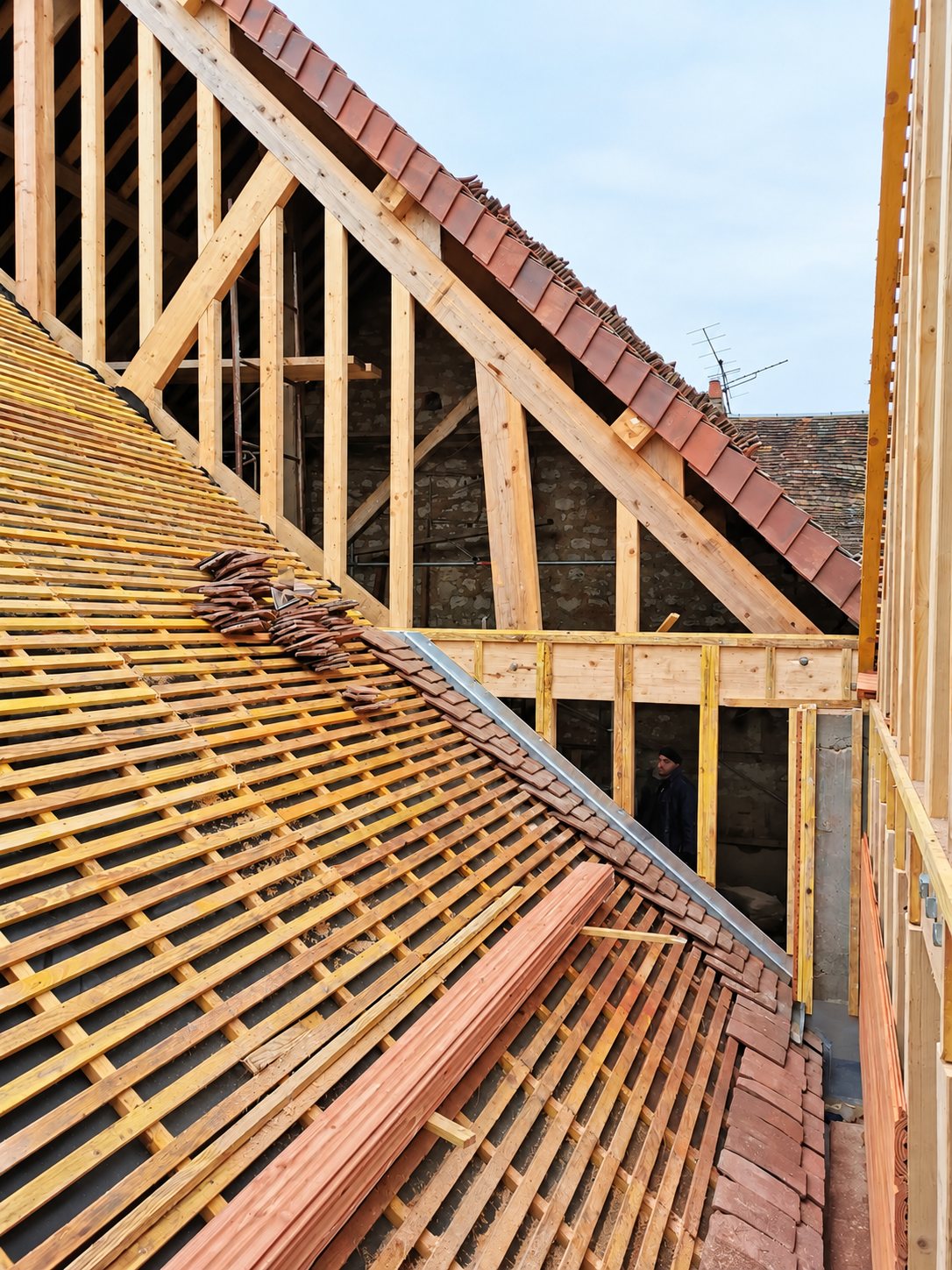 Vue d'un chantier de toiture en cours avec charpente en bois apparente, liteaux posés et anciennes tuiles plates en cours de dépose ou de repose.