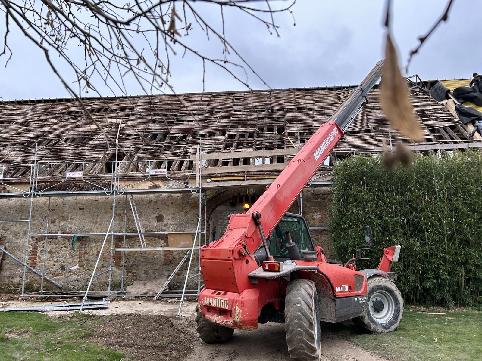 Télescopique Manitou rouge devant une grange en pierre dont la toiture est en rénovation